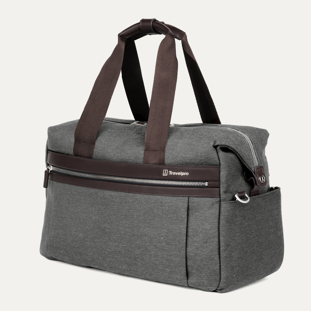 a three-quarter perspective view of the vintage grey travelpro platinum elite underseat tote, highlighting the textured grey fabric, brown leather trim, front zippered pocket, and side accessory pocket.
