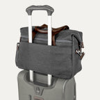 a vintage grey travelpro platinum elite underseat tote stacked on top of a grey rolling suitcase, with its integrated rear trolley strap securely slid over the luggage extension handle for easy transport.