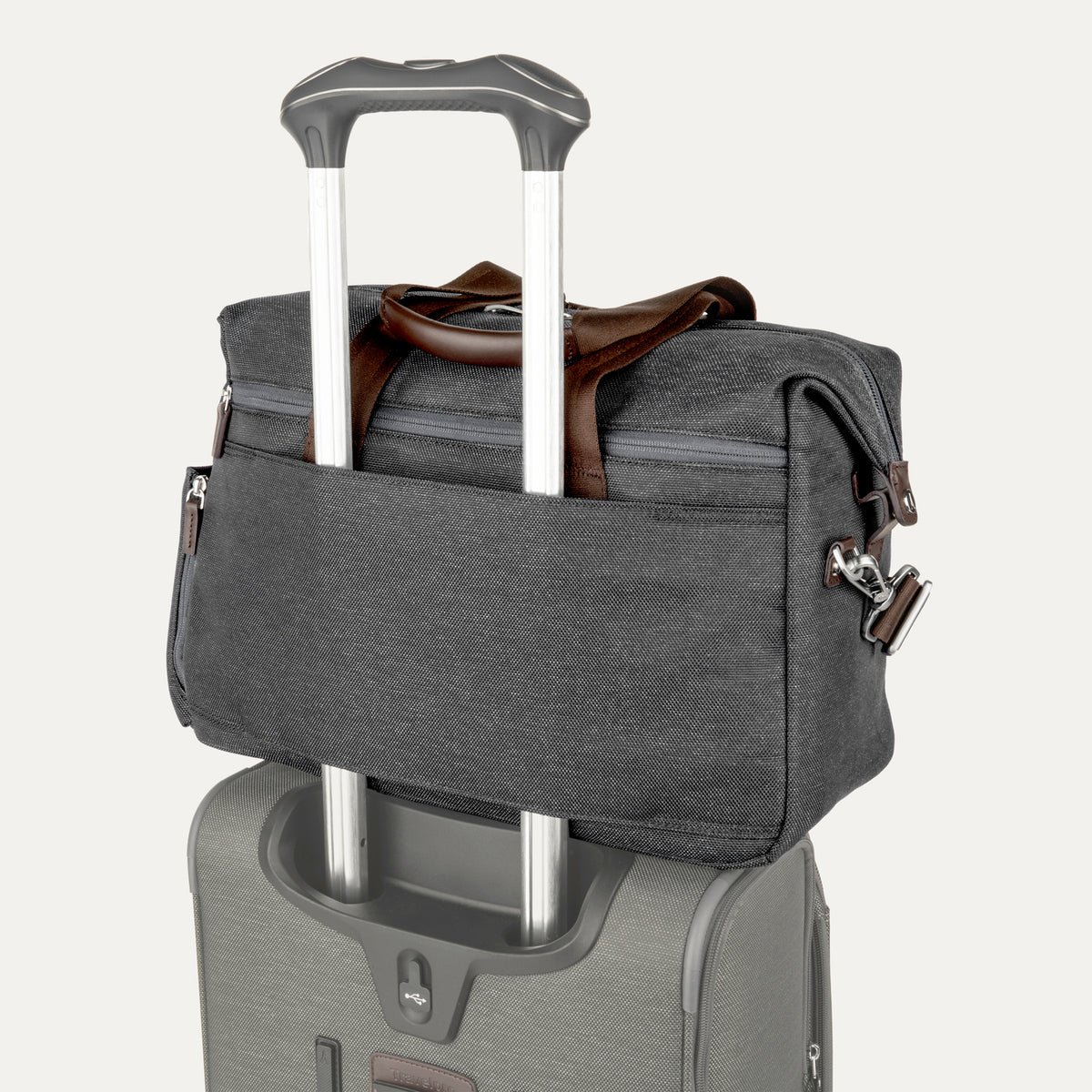 a vintage grey travelpro platinum elite underseat tote stacked on top of a grey rolling suitcase, with its integrated rear trolley strap securely slid over the luggage extension handle for easy transport.